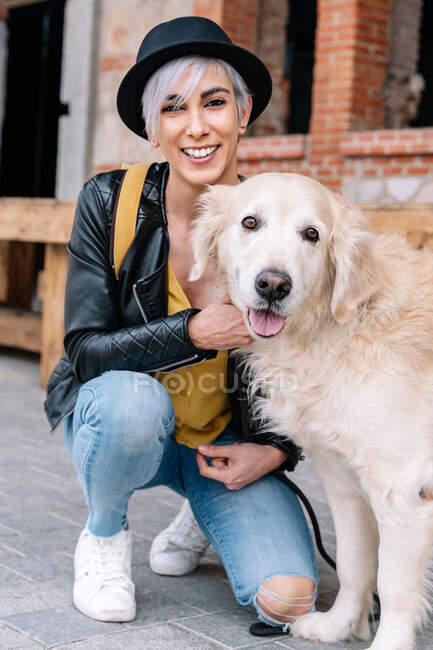Blond female with purebred dog looking at camera while crouching on urban pavement — Stock Photo