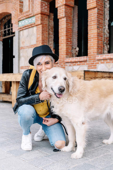 Donna bionda con cane di razza pura che guarda la fotocamera mentre accovacciato sul marciapiede urbano — Foto stock