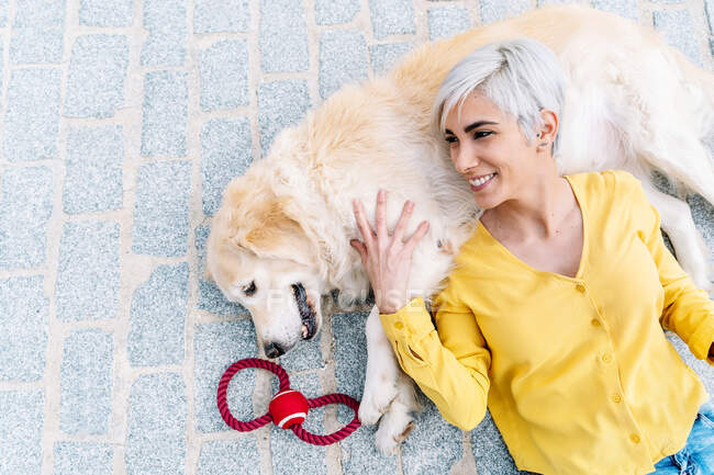 From above smiling young female lying down on charming purebred dog on pavement in daylight — Stock Photo