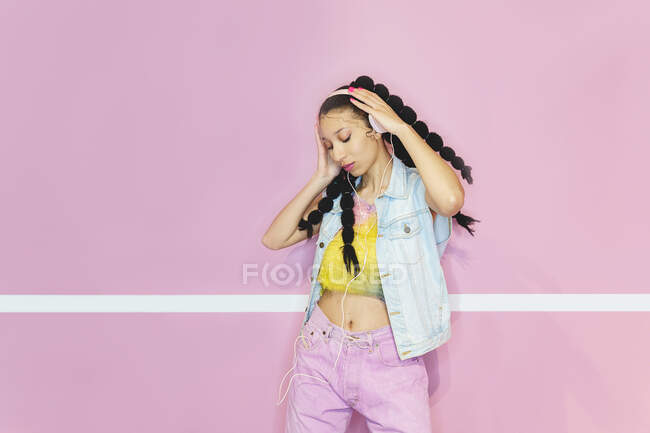 Cool mujer afroamericana en ropa colorida escuchando música en auriculares  mientras disfruta de canciones con los ojos cerrados en el estudio —  individualidad, entretener - Stock Photo | #511443190