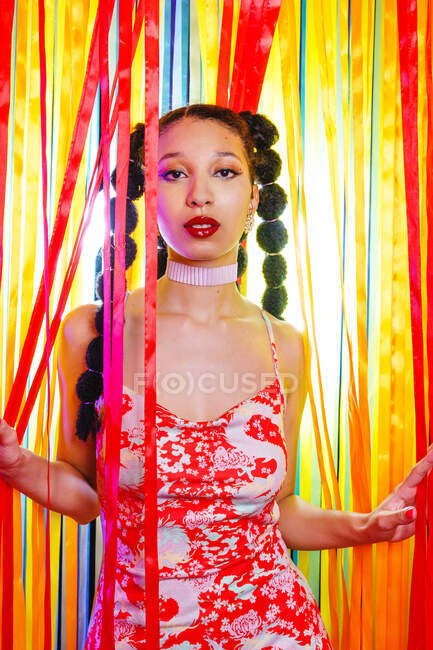 Femme afro-américaine confiante et à la mode en robe debout près de rayures colorées remise en studio et regardant la caméra — Photo de stock
