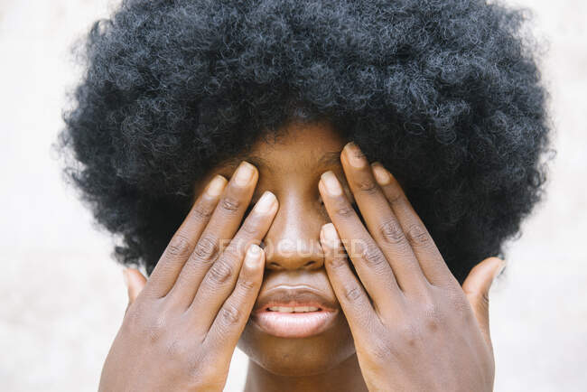 Crop junge afroamerikanische Dame mit lockigen dunklen Haaren bedeckt Augen mit Händen vor weißem Hintergrund — Stockfoto