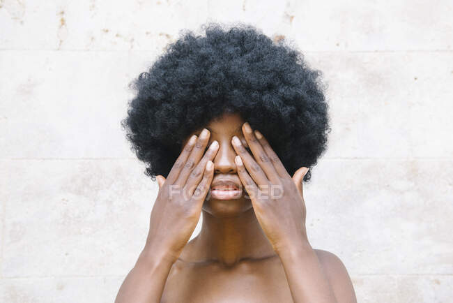 Crop young African American lady with curly dark hair covering eyes with hands against white background — Stock Photo