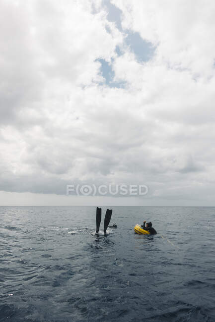 Unrecognizable person with flippers underwater near yellow buoy floating of calm sea water under overcast sky on Lanzarote island — Stock Photo