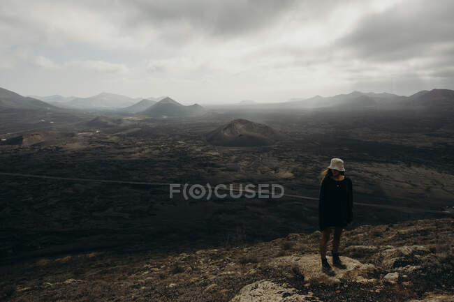 Desde lo alto explorador irreconocible de pie en la colina y admirando increíbles paisajes de montañas en Lanzarote - foto de stock