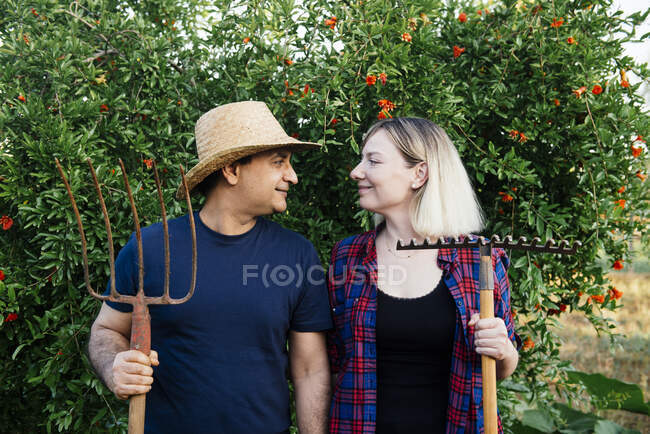 Feliz pareja de granjeros multiétnicos adultos con ropa casual sonriendo y  mirándose el uno al otro