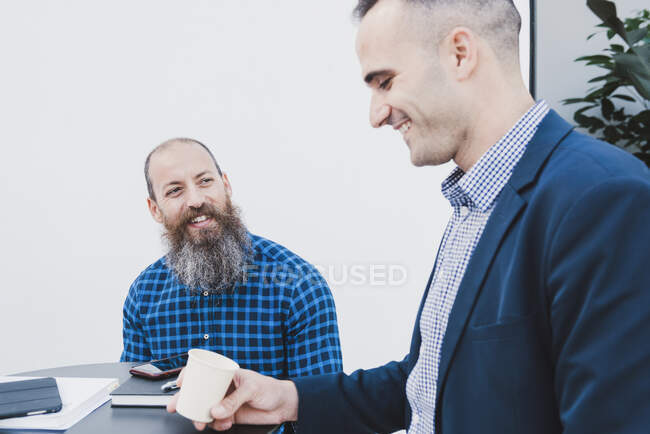 Positive male coworkers sitting at table in office and enjoying coffee break during workday — Stock Photo