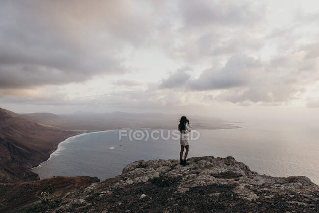 Повернення до нерозпізнаної жінки - мандрівника, що стоїть на скелястому пагорбі і милується захопливим видом на море в бінокль під час відпустки на Лансароте. — стокове фото