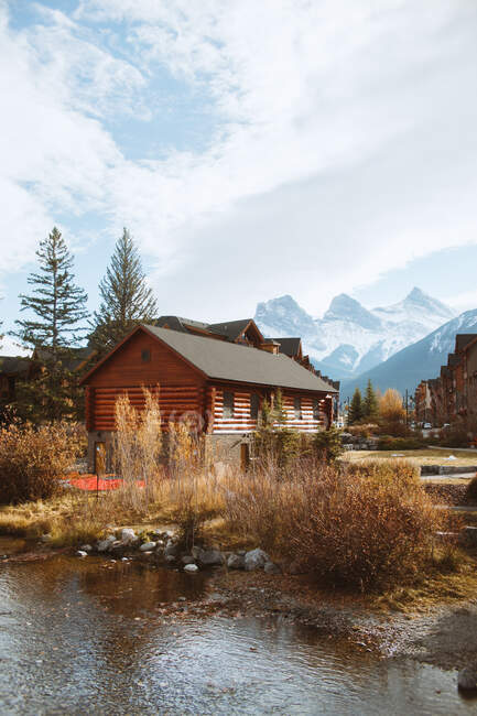 Paisagem outonal pitoresca com casas de madeira localizadas perto do rio contra montanhas nevadas na cidade de Canmore, perto do Parque Nacional Banff do Canadá — Fotografia de Stock