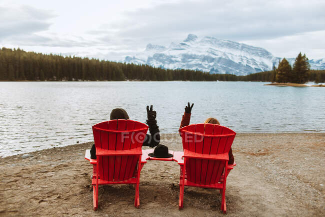 Anonymous tourists showing V sign while resting on red deckchairs on shore of Two Jack Lake in Banff National Park — Stock Photo