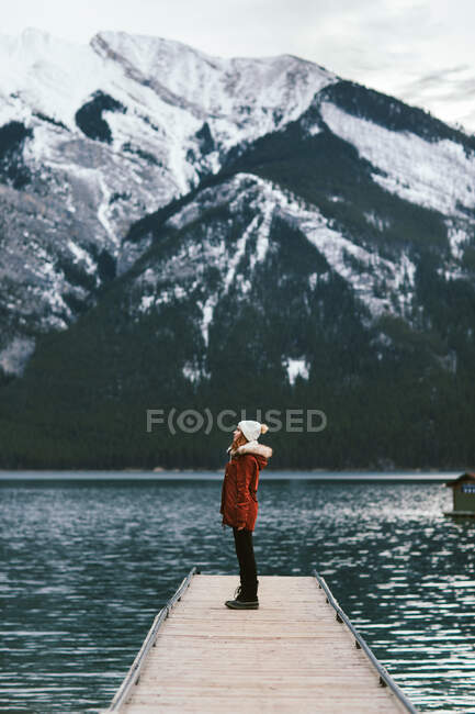 Side view of female traveler standing on quay of Lake Minnewanka against snowy mountain ridge in Banff National Park — Stock Photo