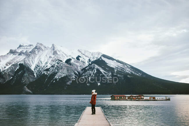 Side view of female traveler standing on quay of Lake Minnewanka against snowy mountain ridge in Banff National Park — Stock Photo