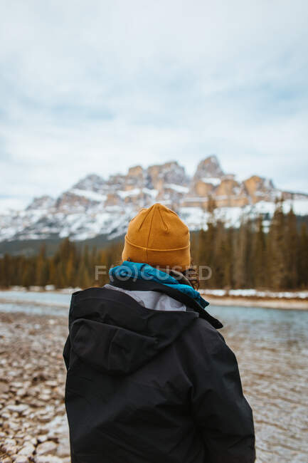 Vista posteriore di un viaggiatore anonimo che ammira il castello innevato Montagna e conifere mentre si trova sulla costa del fiume nel Parco Nazionale di Banff — Foto stock