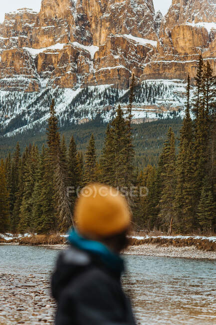Verschwommener anonymer Reisender bewundert verschneiten Burgberg und Nadelbäume, während er an der Flussküste im Banff National Park steht — Stockfoto
