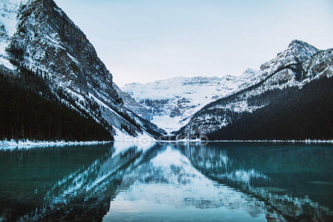 Чиста вода з мирного озера Луїза віддзеркалює сніжний гірський хребет і хмарне небо в зимовий день в Альберті (Канада). — стокове фото