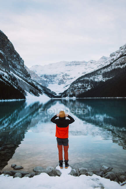 Blick zurück auf einen anonymen Reisenden, der an der verschneiten Küste des friedlichen Lake Louise steht und an einem Wintertag die Berge im Banff National Park bewundert — Stockfoto