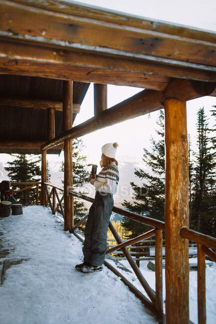 Une voyageuse prend une boisson chaude au thermos pendant qu'elle se repose dans un abri en bois près des montagnes enneigées du parc national Banff — Photo de stock