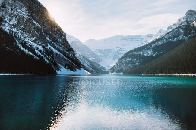 Água limpa do tranquilo Lago Louise refletindo cume de montanha nevado e céu nublado no dia de inverno em Alberta, Canadá — Fotografia de Stock