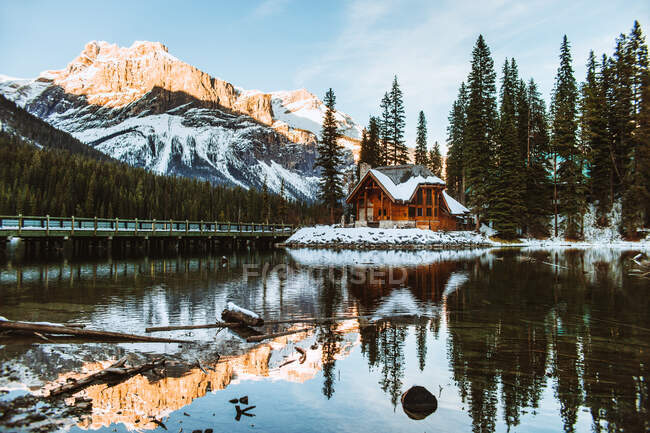 Long bridge crossing Emerald Lake near wooden cottage located near coniferous forest and snowy mountain on winter day in British Columbia, Canadá — Fotografia de Stock