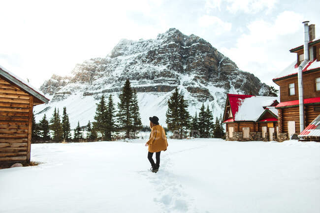 Rückansicht einer unkenntlich gemachten trendigen Frau, die an einem Wintertag in Alberta, Kanada, in der Nähe einer Holzhütte am Ufer des Bow Lake spazieren geht — Stockfoto