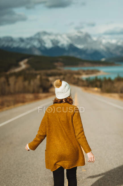 Visão traseira de turista feminina irreconhecível em roupas casuais andando na David Thompson Highway perto do lago abraham contra montanhas nevadas em Alberta, Canadá — Fotografia de Stock