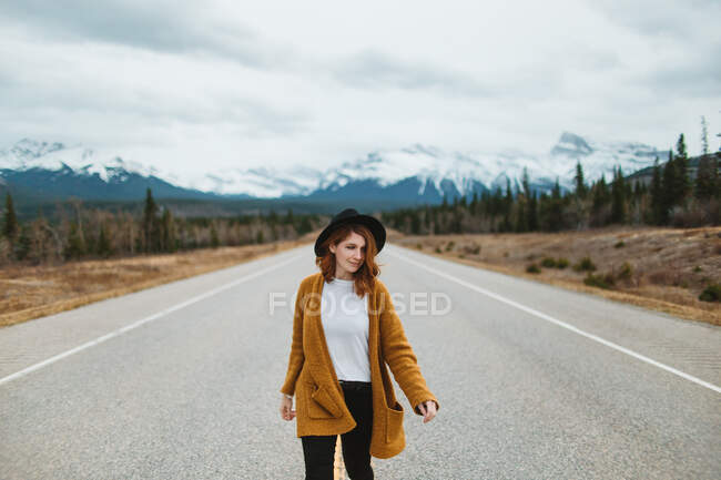 Turista donna in abiti casual che cammina sulla David Thompson Highway contro le montagne innevate in Alberta, Canada — Foto stock