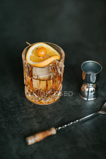 Composition of cold icy whiskey garnished with lemon slice and placed on black table near jigger — Stock Photo