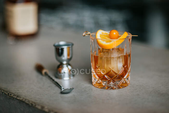 Composizione di whisky freddo ghiacciato guarnito con fetta di limone e posto sul tavolo di cemento vicino al jigger — Foto stock