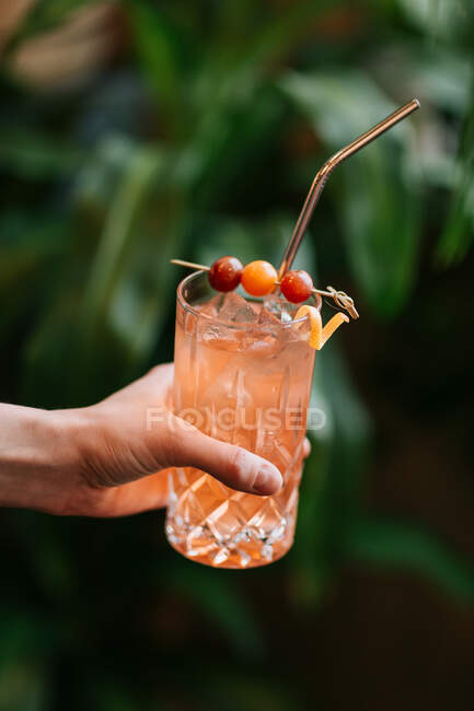Crop anonyme Person demonstriert transparentes Glas mit kalten Cocktail mit Eiswürfeln serviert mit Beeren am Stiel und null Abfall Stroh — Stockfoto