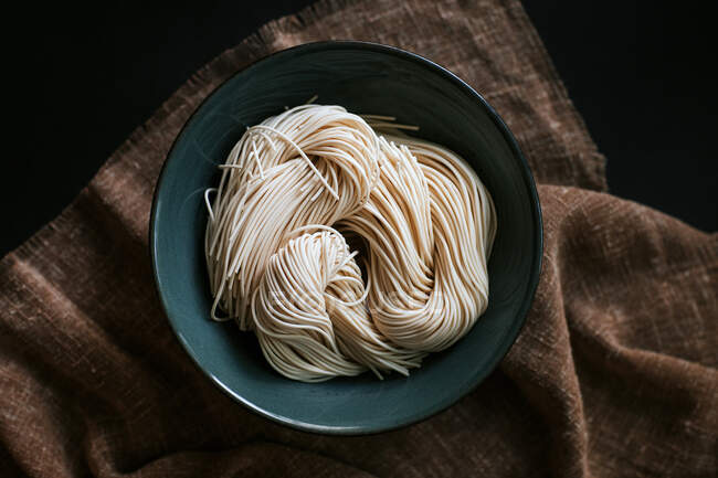 Draufsicht auf ungekochte Nudeln zur Ramen-Zubereitung in Schüssel auf braunem Tischtuch — Stockfoto