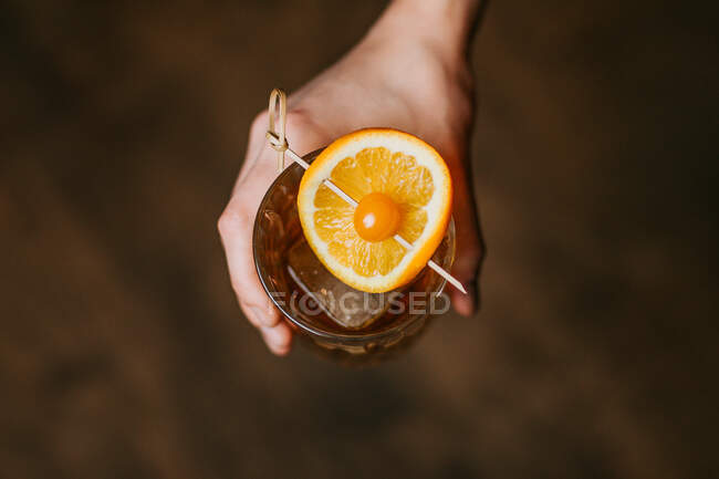 Зверху врожаю анонімний людина зі склянкою віскі з кубиками льоду і палицею з апельсином і ягодою — стокове фото
