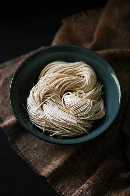 Draufsicht auf ungekochte Nudeln zur Ramen-Zubereitung in Schüssel auf braunem Tischtuch — Stockfoto