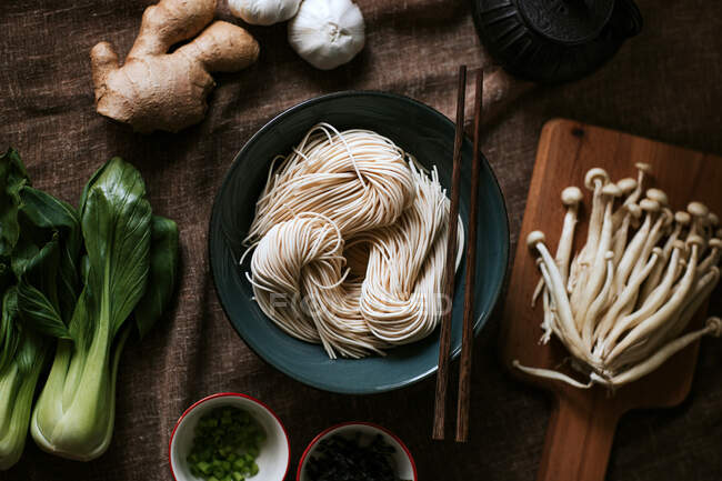 Top view of assorted ingredients for tasty ramen preparation placed on brown tablecloth in kitchen — Stock Photo
