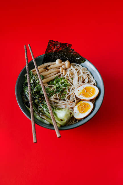 Top view of ceramic bowl with delicious ramen and chopsticks placed on red background — Stock Photo