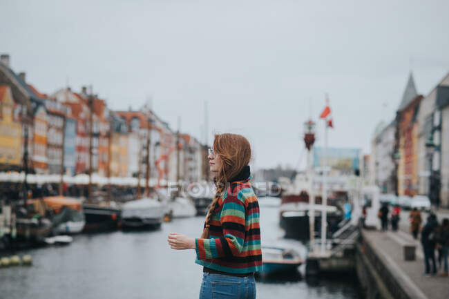 Бічний вид на жінку, що стоїть проти човнів, пришвартованих на березі каналу в Копенгагені. — стокове фото