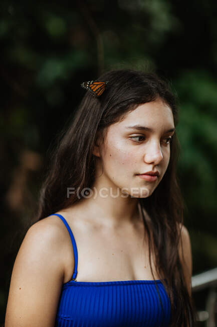 Ruhige junge Frau im Bikini mit Zierschmetterlingen auf den Haaren, die während des Sommerabenteuers in Costa Rica vor verschwommenem grünem Laub stehen — Stockfoto