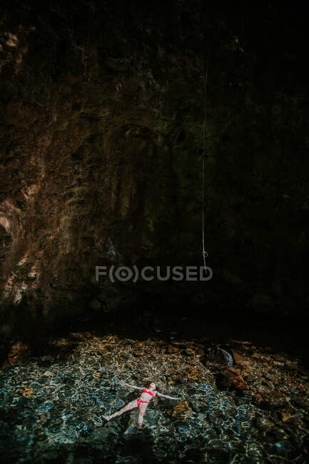 Von oben eine unkenntlich entspannte Reisende im Bikini, die auf der Wasseroberfläche eines klaren, transparenten Pools in der Nähe einer Felshöhle liegt, während sie ihren Sommerurlaub im Nationalpark Rincon de la Vieja in Costa Rica genießt — Stockfoto