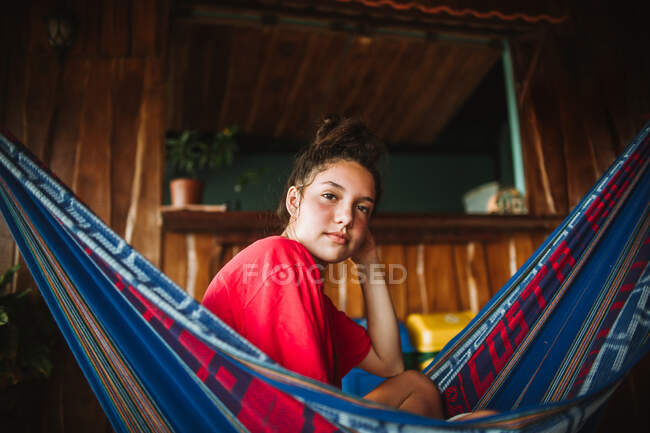 Vista laterale del giovane viaggiatore sereno in bikini guardando la macchina fotografica che si rilassa in amaca appesa sulla terrazza della casa tropicale durante le vacanze estive nella città di Uvita in Costa Rica — Foto stock