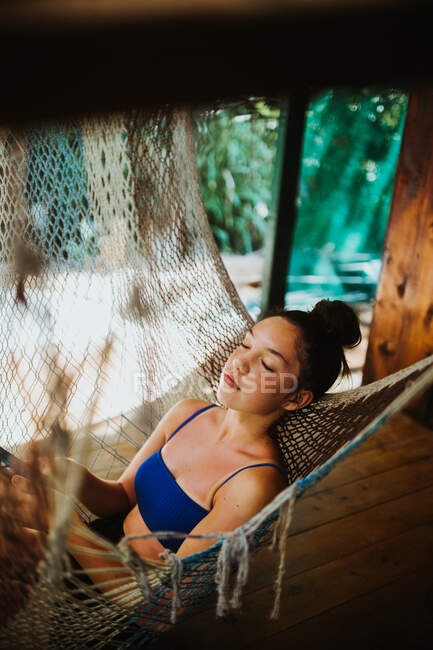 Side view of serene young female traveler in bikini chilling in hammock hanging on terrace of tropical house during summer holidays in Uvita town in Costa Rica — Stock Photo