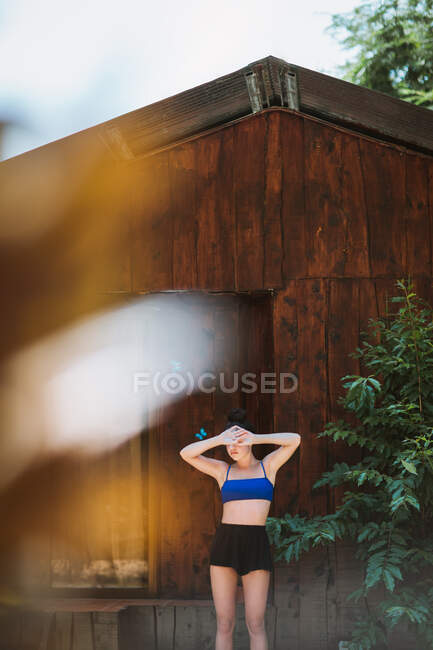 Jeune voyageuse méconnaissable en maillot de bain debout couvrant le visage avec les mains près de la maison en bois avec des papillons bleus assis sur le mur pendant les vacances d'été au Costa Rica — Photo de stock