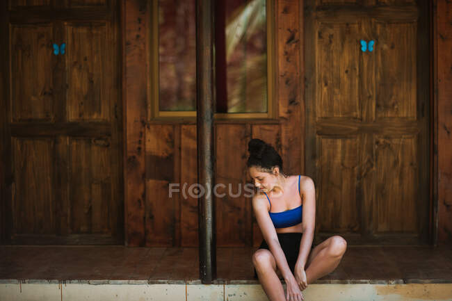 Jovem viajante encantadora em trajes de banho sentado perto da casa de madeira com borboletas azuis sentadas na parede enquanto passa férias de verão na Costa Rica — Fotografia de Stock