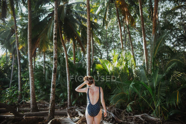 Back view of peaceful unrecognizable young female in swimwear standing with hands on head and eyes closed against tall green palms during summer holidays on seacoast of Costa Rica — Stock Photo