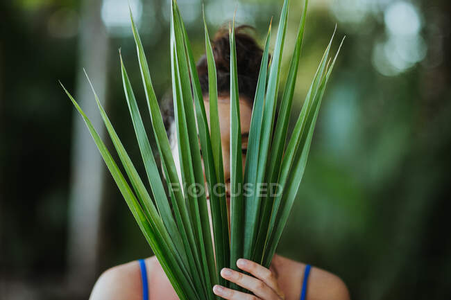 Serene female covering face with green leaves of palm tree in summer in Uvita — Stock Photo