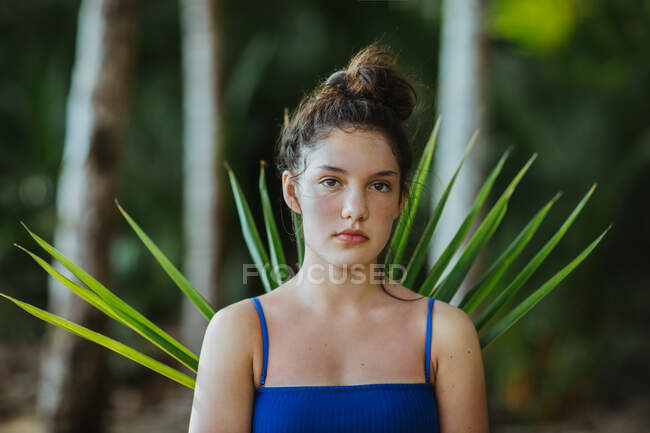 Спокойная женщина стоит с зеленой пальмовой веткой в тропическом саду в Uvita и смотрит в камеру — стоковое фото