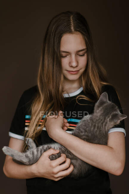 Dreamy teenage girl holding fluffy cute cat on brown background in studio — Stock Photo