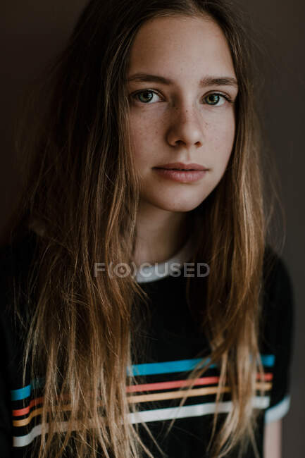 Чарівна дівчина-підліток з довгим волоссям дивиться на камеру на темному тлі в студії — стокове фото