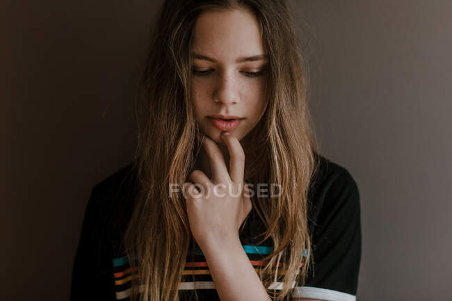 Thoughtful charming teen girl with long hair looking down on dark background in studio — Stock Photo