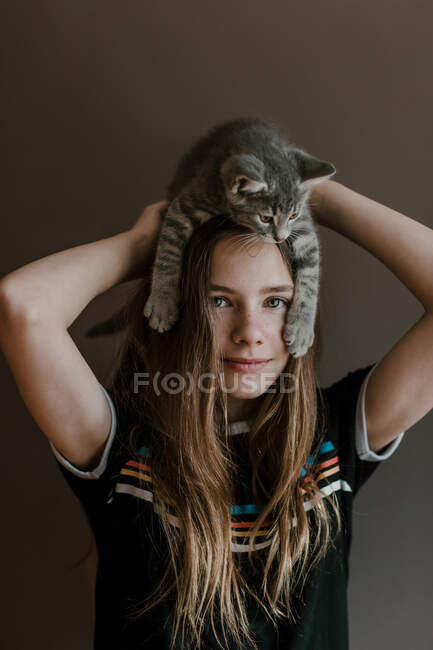 Verträumte Teenager-Mädchen mit flauschigen süßen Katze auf dem Kopf auf braunem Hintergrund im Studio — Stockfoto