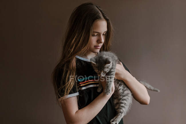 Мечтательная девочка-подросток держит пушистую милую кошку на коричневом фоне в студии — стоковое фото