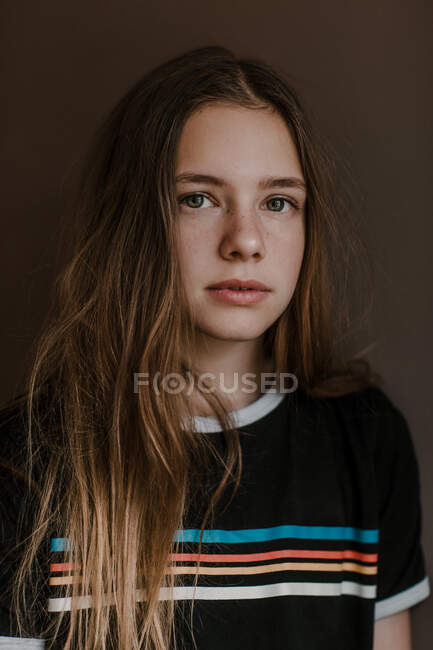 Charming teen girl with long hair looking at camera on dark background in studio — Stock Photo